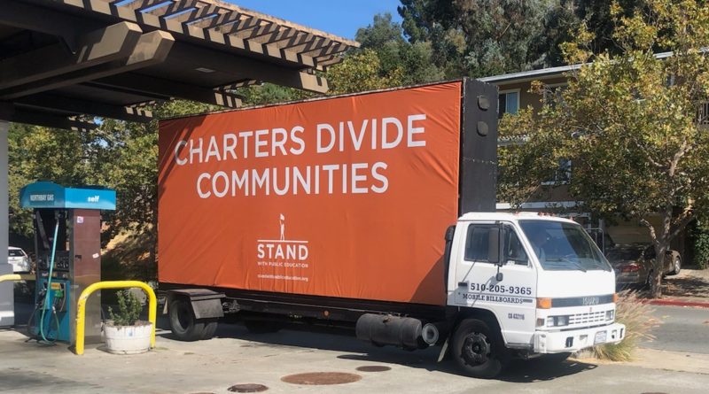 Orange billboard truck bearing message "Charters Divide Communities"